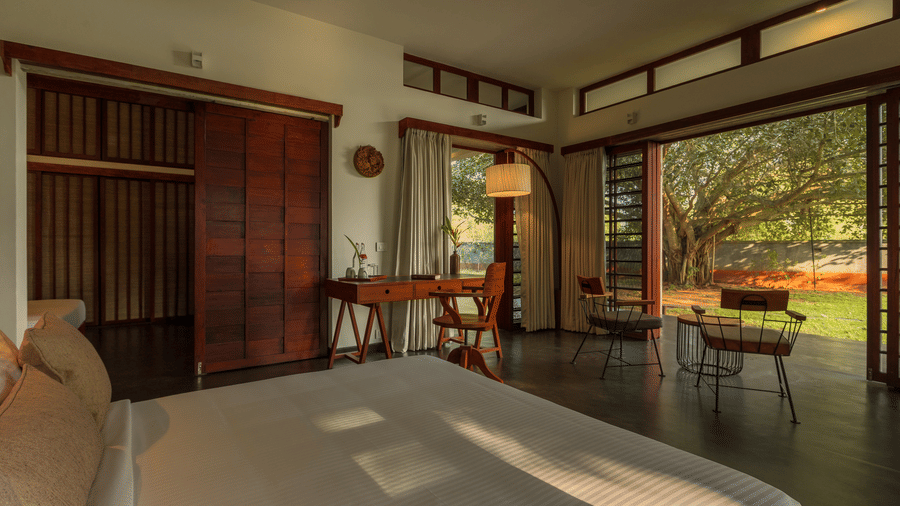 Villa Wuwei at Mango Hill Auroville, Pondicherry featuring an indoor lounge has a table and chairs, with large windows offering a view of the garden.
