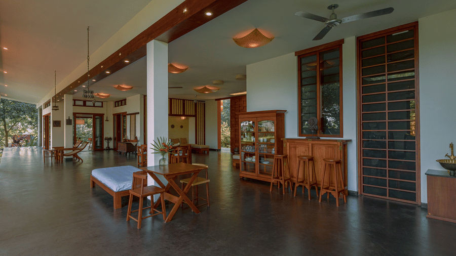 Villa Wuwei in Mango Hill Auroville, Pondicherry featuring a corridor with tables and chairs runs alongside a wall with openings and extends into a seating area.