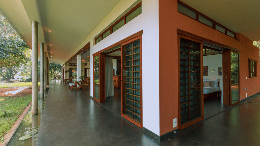 Villa Wuwei at Mango Hill Auroville, Pondicherry featuring a walkway runs along a building with doors and windows opening into rooms and a railing lines the outer edge.
