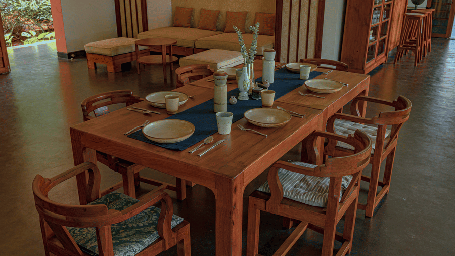 Villa Wuwei at Mango Hill Auroville, Pondicherry featuring a long wooden dining table set with plates and bowls is surrounded by six wooden chairs in an open-plan room.