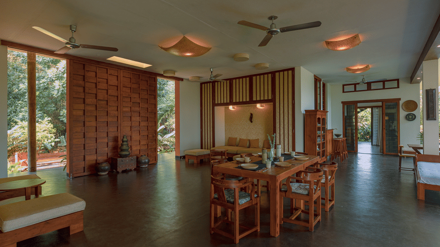 Villa Wuwei at Mango Hill Auroville, Pondicherry featuring a large room contains a dining set and a seating area with a brick wall and ceiling fans.