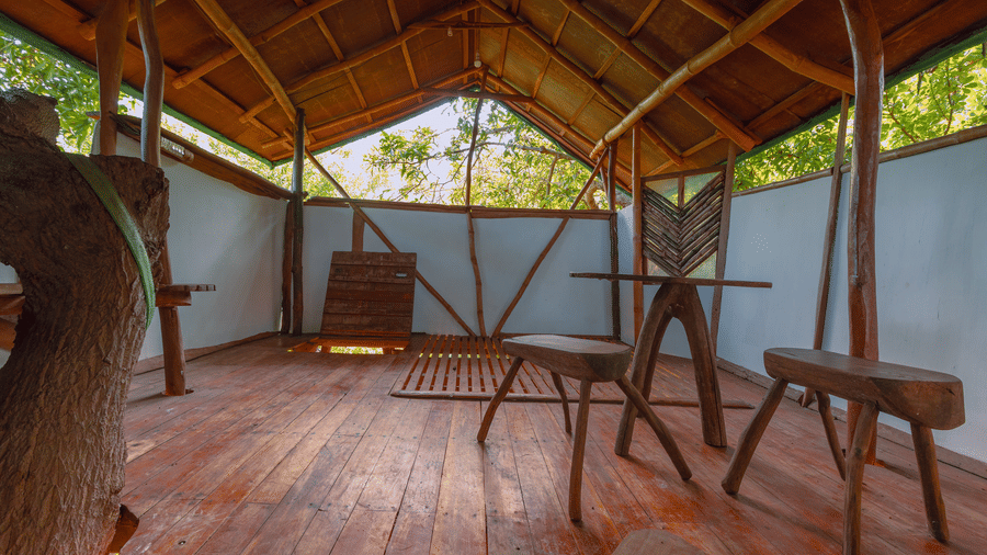 Interiors of a tree house in Villa Wuwei at Mango Hill Auroville, Pondicherry featuring a swing chair and a small bench under a roof made of natural materials.