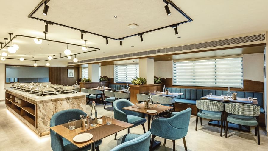 A wide shot of the restaurant at Mango Hill Central, Chennai, showing tables with blue chairs and a buffet area.