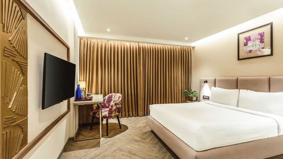 A wide-angle view of a room with a large bed and a television at Mango Hill Central, Chennai. A desk and chair are visible on the right.