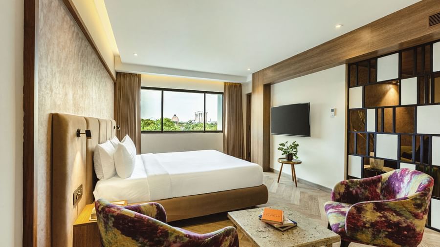A wide-angle view of a room with a large bed and a seating area at Mango Hill Central, Chennai. A TV is on the far wall.