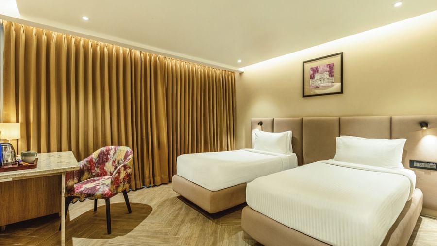 A wide shot of a twin-bedded room at Mango Hill Central, Chennai. A desk is on the left, and a wooden slat wall is behind the beds.