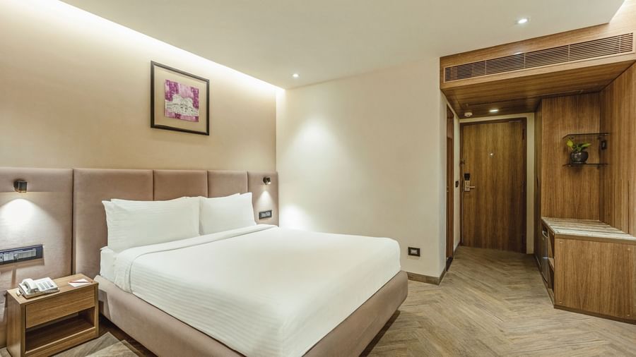A wide-angle view of a room with a large bed at Mango Hill Central, Chennai. The room has a wooden wall feature.
