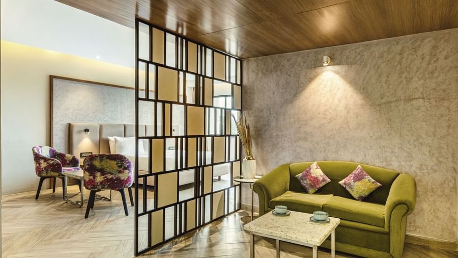 A seating area in a suite at Mango Hill Central, Chennai, with a green sofa and two purple chairs. A divider separates the seating from the rest of the room.