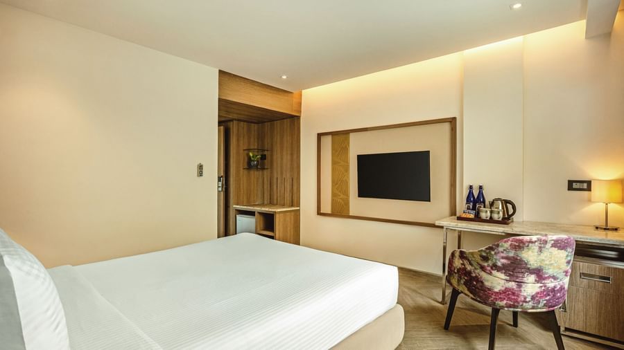 A wide-angle view of a room with a bed and a television at Mango Hill Central, Chennai. A desk with a chair is in the foreground.