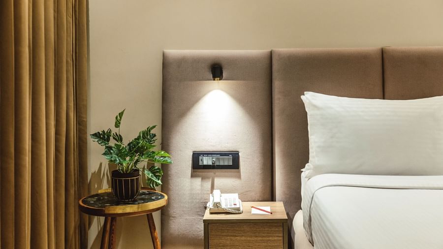 A close-up of a bed with a plant on a bedside table in a room at Mango Hill Central, Chennai.