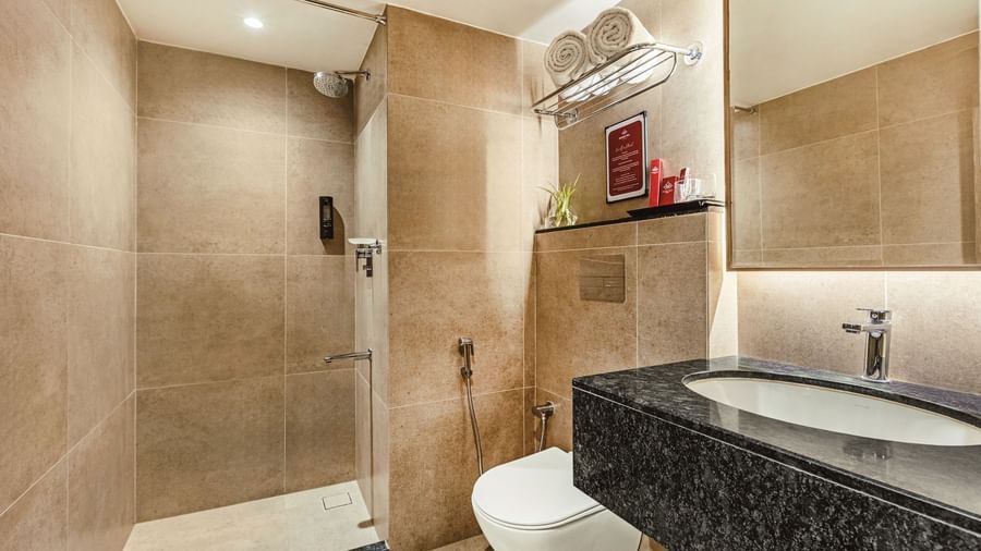 A bathroom at Mango Hill Central, Chennai, with a black-topped sink, toilet, and shower area visible.