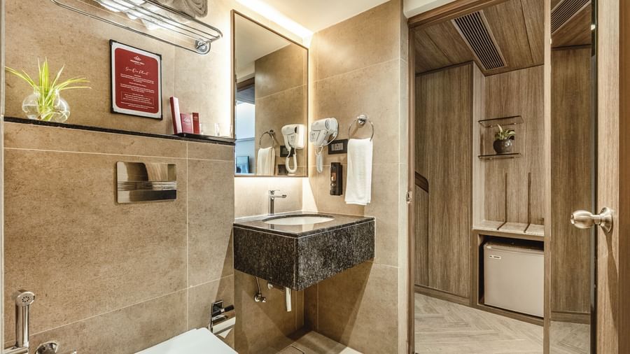 A wide view of the bathroom at Mango Hill Central, Chennai, showing the toilet, sink, and shower area.