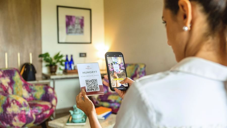 A person sitting at a desk and taking a photo of a QR code on a card in a room at Mango Hill Central, Chennai.
