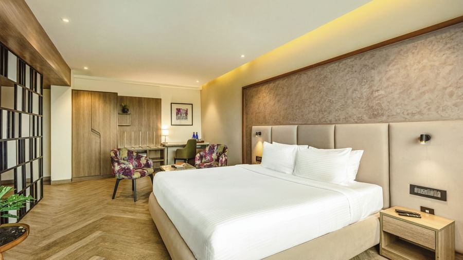 A wide-angle view of a room with a large bed at Mango Hill Central, Chennai. A desk and a chair are visible on the left.