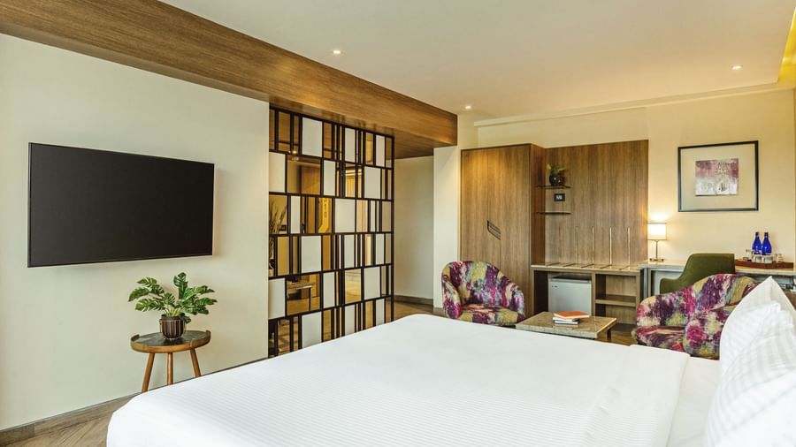  A wide-angle view of a room with a large bed and a television at Mango Hill Central, Chennai. A desk and chair are on the left.
