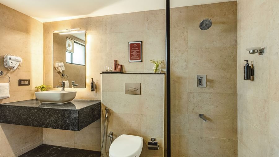 A bathroom at Mango Hill Central, Chennai, with a sink, a toilet, and a walk-in shower area.