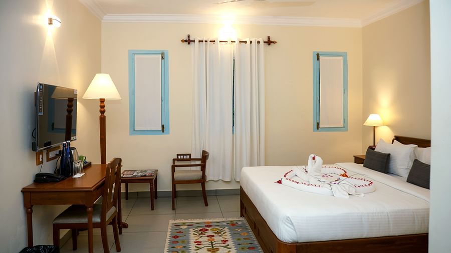 A suite with a large bed, flat screen TV, table and chair, and three lamps of different sizes | Mango Hill La Serene, Pondicherry