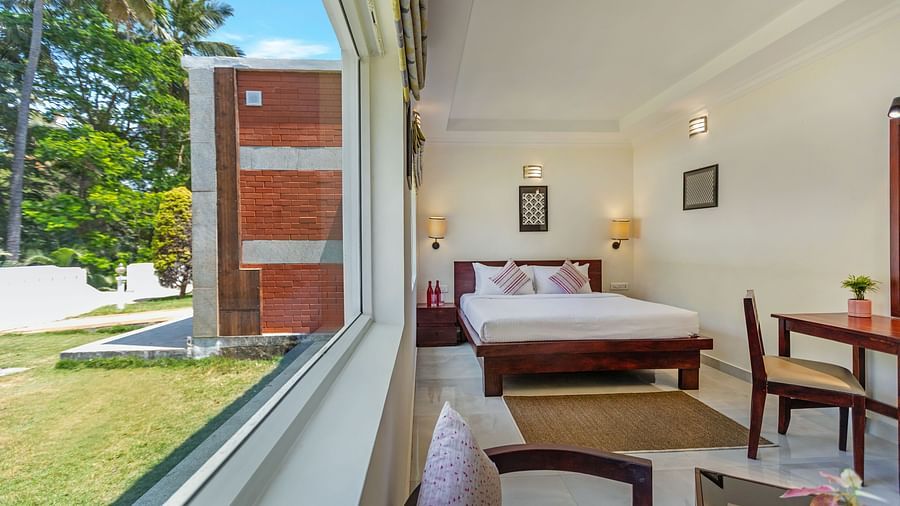 A bright hotel room with a bed, seen through a large window overlooking a garden with palm trees - Mango Hill Resort, Coimbatore