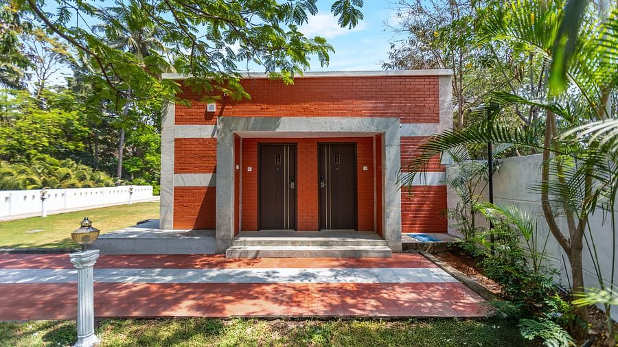 A building with two brown doors, red brick walls, and grey concrete trim, surrounded by a green lawn and trees - Mango Hill Resort, Coimbatore