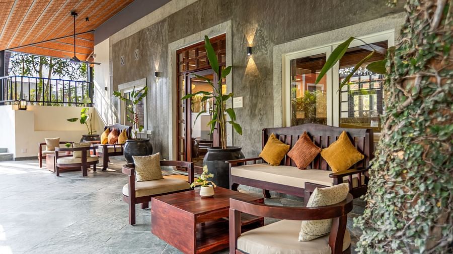 A covered patio with dark wood furniture, potted plants, and a textured ceiling - Mango Hill Resort, Coimbatore