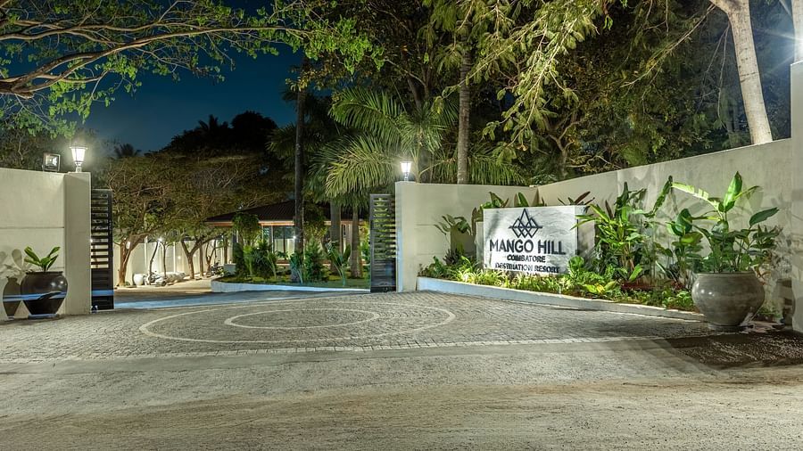 The entrance to Mango Hill Resort, Coimbatore, featuring a white gate with a sign and trees on either side