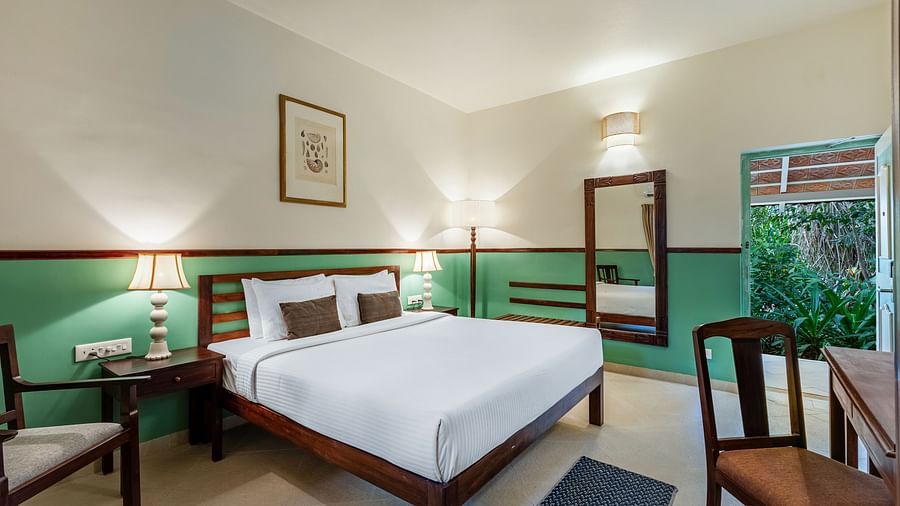 Comfortable bedroom with a wooden bed frame, white linens, bedside lamps, a framed picture, and a window with draped curtains | Mango Hill Shallow Beach Resort ECR