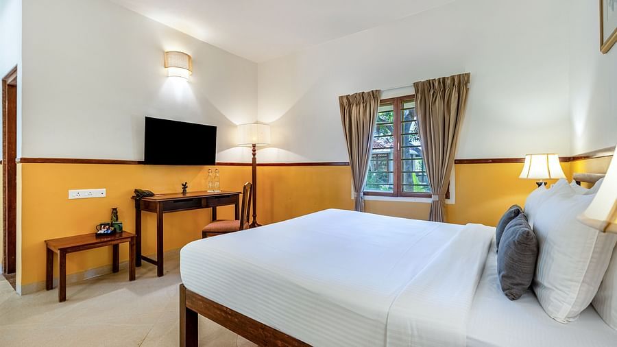 Well-lit bedroom with a wooden bed frame, white linens, a desk and chair, a flat-screen TV, and a window with drapes| Mango Hill Shallow Beach Resort ECR