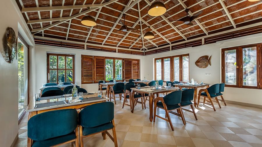 Wide angle shot of restaurant dining area with wooden tables, blue chairs, and a high, patterned ceiling | Mango Hill Shallow Beach Resort ECR