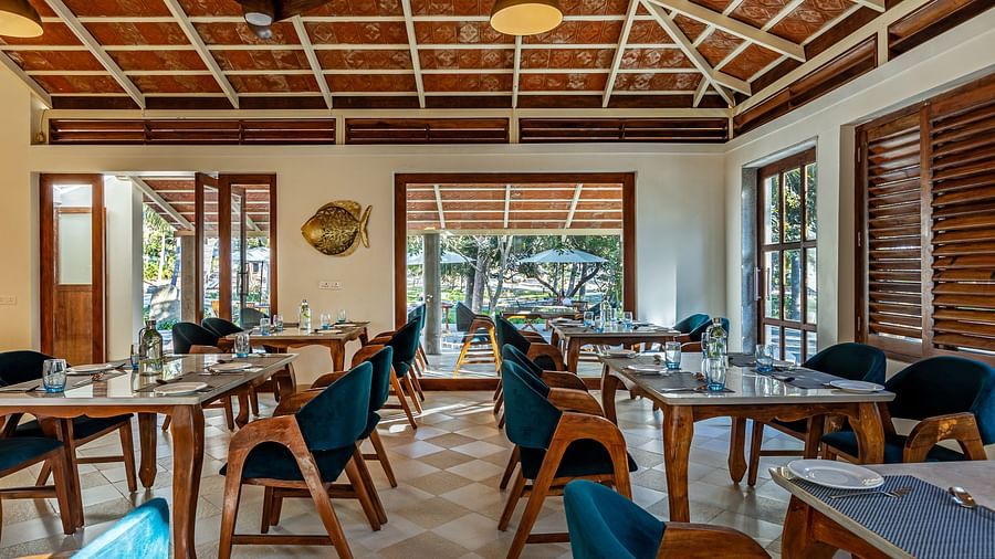 Image of a restaurant by the beach with wooden interiors blue chairs, and a high, patterned ceiling | Mango Hill Shallow Beach Resort ECR