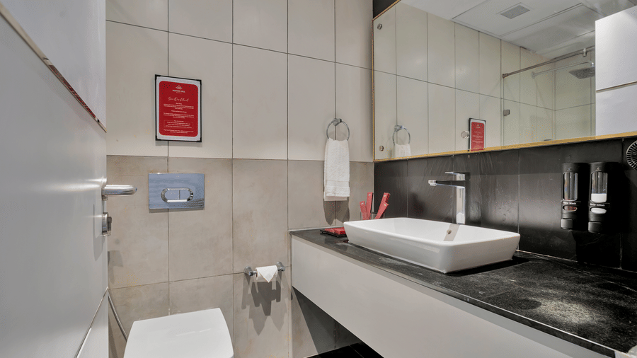 Bathroom in Twin Room at Mango Hill, Velankanni with a sink, mirror, toilet, and towel rack.