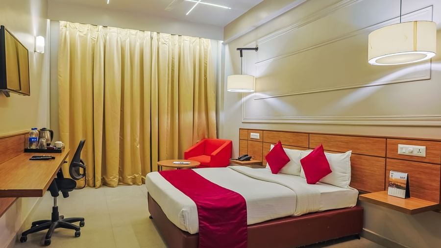 Bedroom with double bed, red runner, pillows, desk and curtains at Max Hotel Prayagraj.