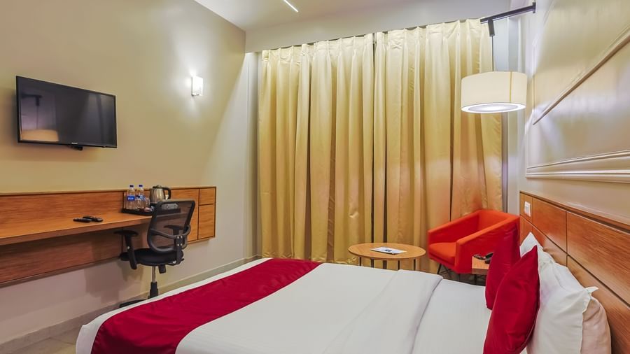 Bedroom with double bed, red runner, pillows, wall-mounted TV and curtains at Max Hotel Prayagraj.