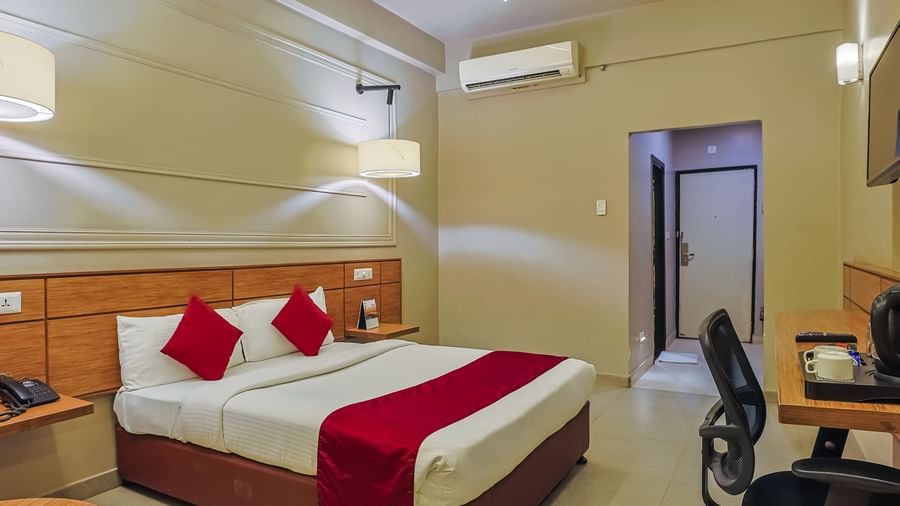 Bedroom with double bed, red runner, pillows, work desk and chair at Max Hotel Prayagraj.
