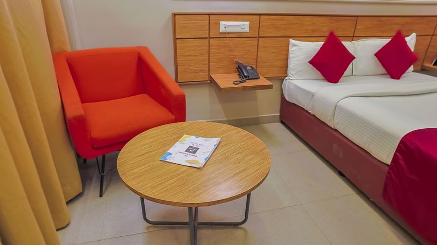 Seating area with orange chair, round table and bedside cabinet at Max Hotel Prayagraj.