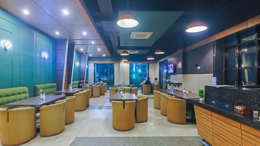 Restaurant with multiple dining tables, green accents and ceiling lights at Max Hotel Prayagraj.