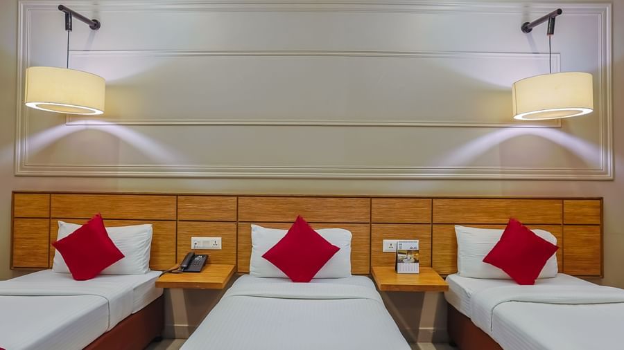 Neat room with three single beds and bright lighting at Max Hotel Prayagraj.