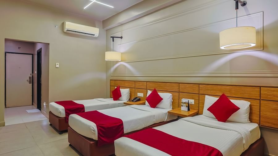 Clean and airy room with three single beds and minimalist decor at Max Hotel Prayagraj.