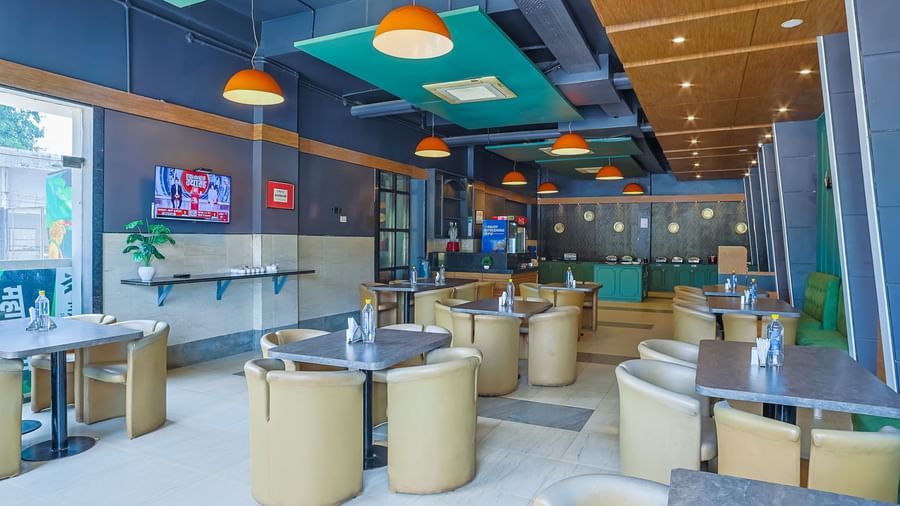 Restaurant with round tables, cushioned chairs and TV on wall at Max Hotel Prayagraj.