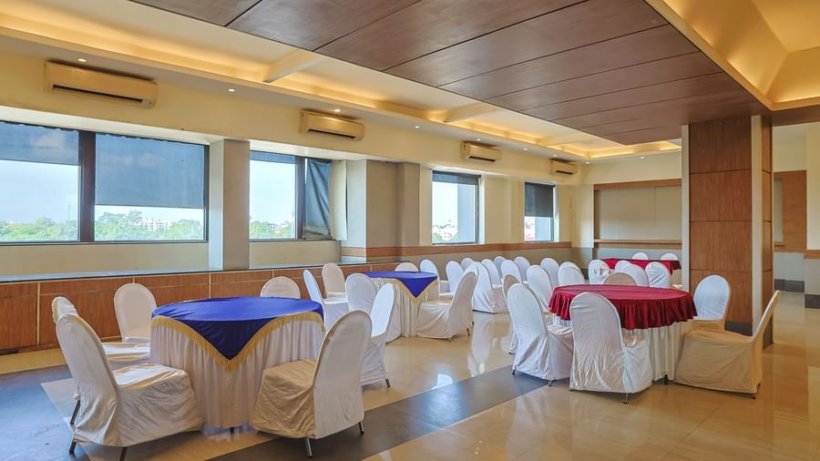 Banquet hall with white chairs, wooden ceiling and bright lighting at Max Hotel Prayagraj.