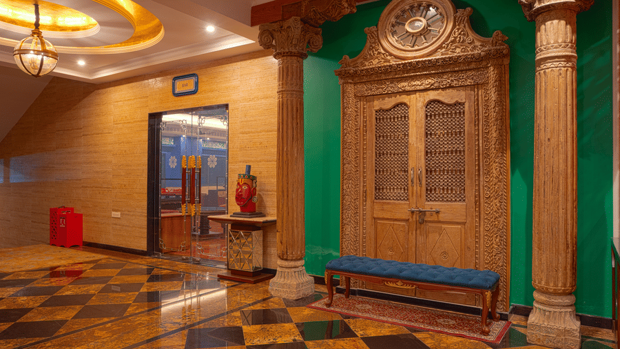 A lobby entrance featuring a large, ornate wooden door, pillars, green wall, and a black and yellow chequered floor at MAYFAIR Bay Resort, Paradeep.