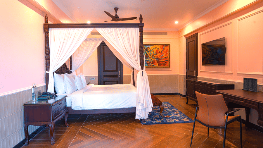 A luxurious 4-poster king size bed with white canopy drapes in a room with wooden floors and contemporary artwork at at MAYFAIR Bay Resort, Paradeep.
