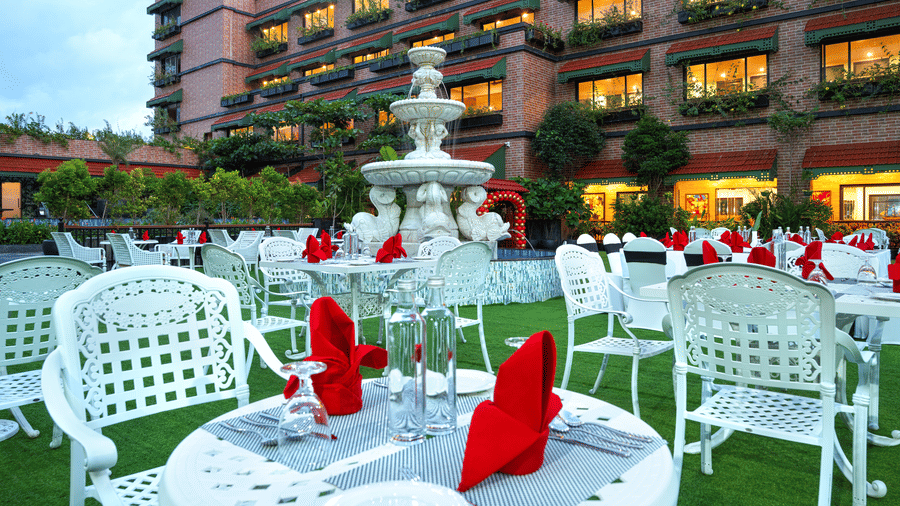 Outdoor event setup on the lawn, showing white lattice tables dressed with red napkins, centred around the fountain at MAYFAIR Bay Resort, Paradeep.