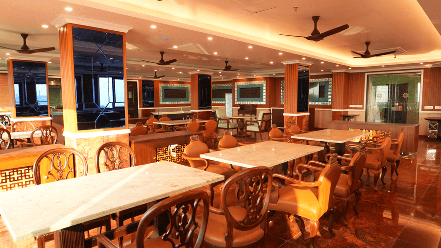 Dining area with long tables, chairs, warm lighting, and a spacious layout inside a restaurant at MAYFAIR Bay Resort, Paradeep.