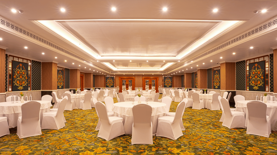 A large, elegant banquet hall with a patterned yellow carpet, set up with multiple circular tables and chairs at MAYFAIR Bay Resort, Paradeep.