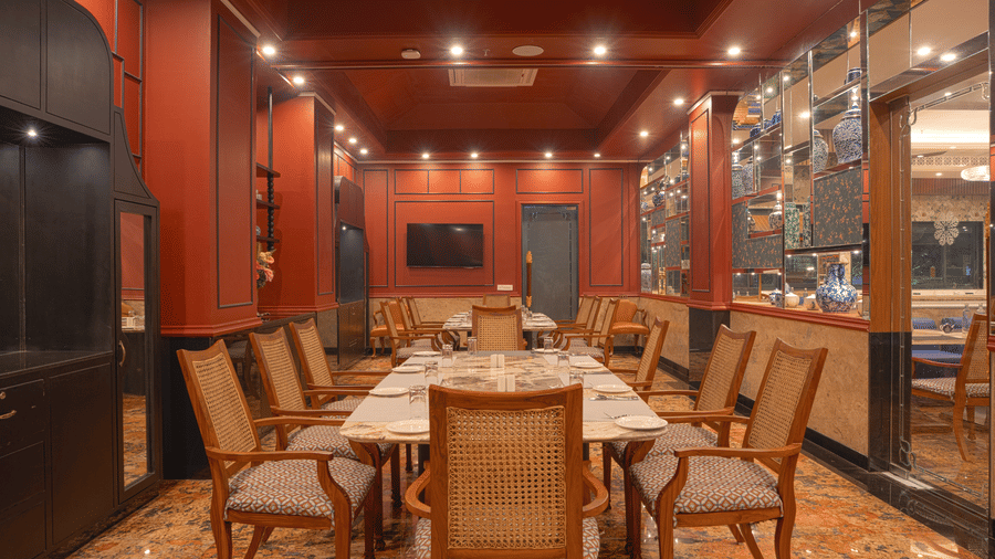 A dining room with a long wooden table set for a meal, surrounded by upholstered chairs and wood-panelled walls at MAYFAIR Bay Resort, Paradeep.