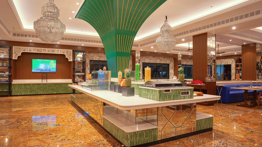 A modern buffet serving area in a large dining hall, featuring marble counters and a distinctive green overhead canopy at MAYFAIR Bay Resort, Paradeep.