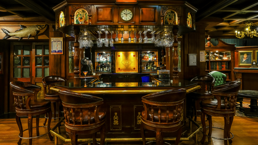 Baron and Baroness bar at MAYFAIR Lagoon, Bhubaneswar featuring a bar counter, liquor bottle in shelves behind the bar, and near the counter top there are chairs placed.