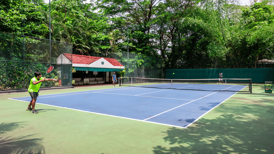 Outdoor tennis court at Mayfair Lagoon, Bhubaneswar, surrounded by lush green trees, offering guests a refreshing sporting experience in a natural setting
