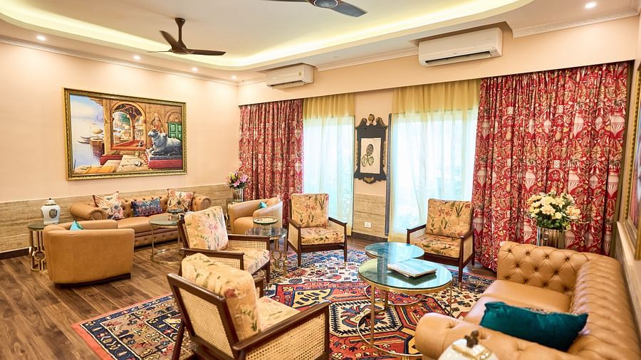  A seating area with plush furniture arranged around the table, curtains drawn to the side, and a wall-mounted painting at Mayfair Manor, Alibag