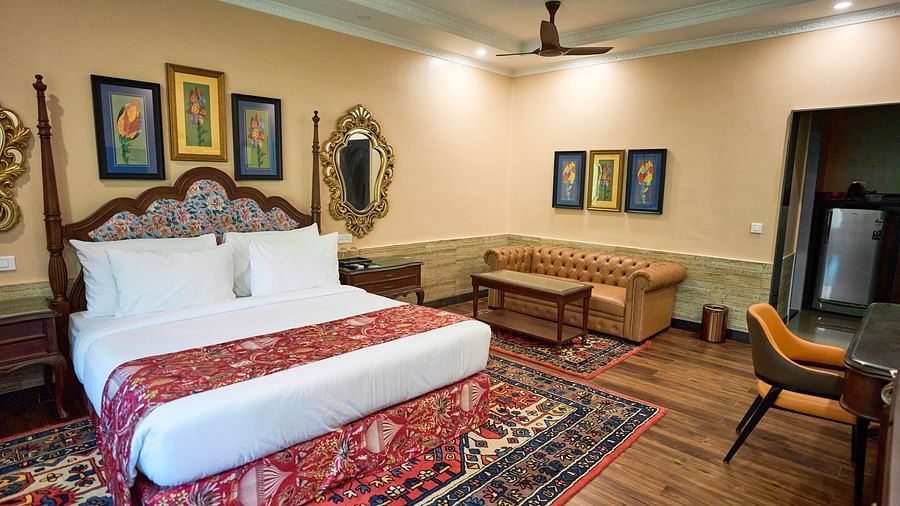 A spacious room with a large bed on one side and cushioned seating furniture on the other, adorned with wall-mounted frames for decoration at Mayfair Manor, Alibag